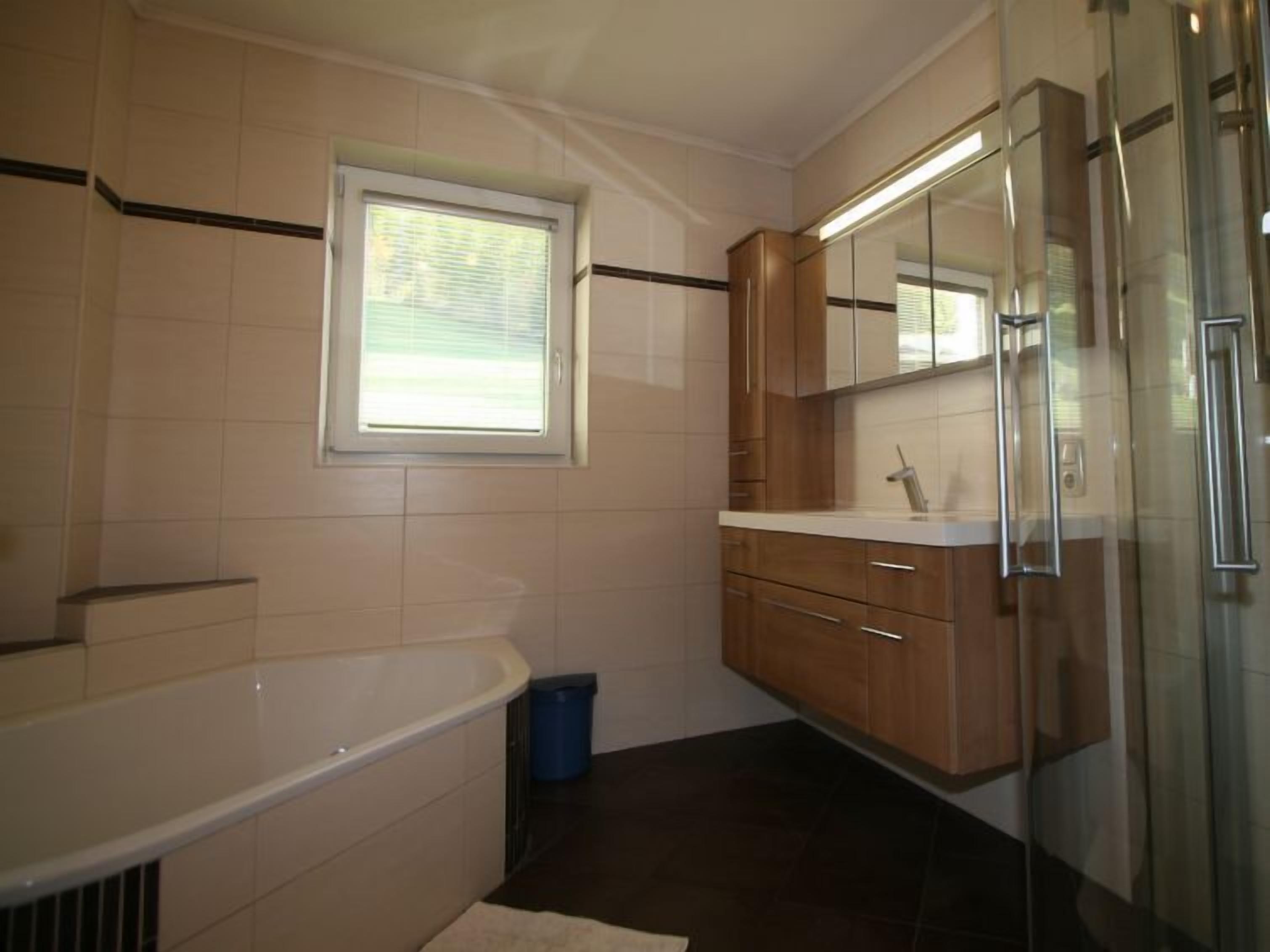 Une salle de bain avec une baignoire, une fenêtre, des meubles en bois et une poubelle.