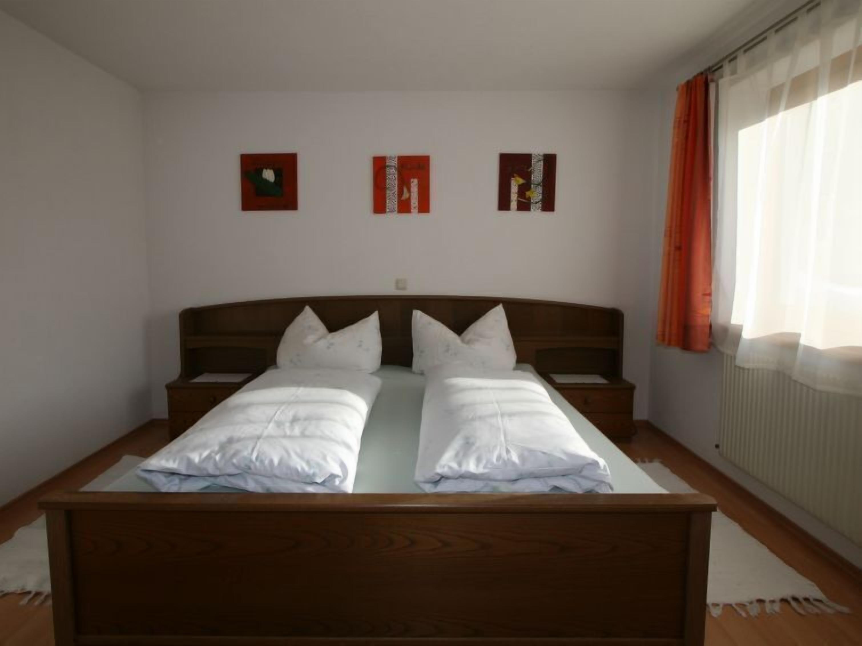 Ein Doppelbett mit Holzkopfseitenverkleidung, zwei Nachttische und ein Fenster mit Vorhängen.