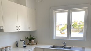 Una cuina moderna amb armaris blancs, un rentapeus d'acer inoxidable i un rentaplats. Hi ha una finestra que deixa passar llum natural i ofereix vistes a l'exterior.