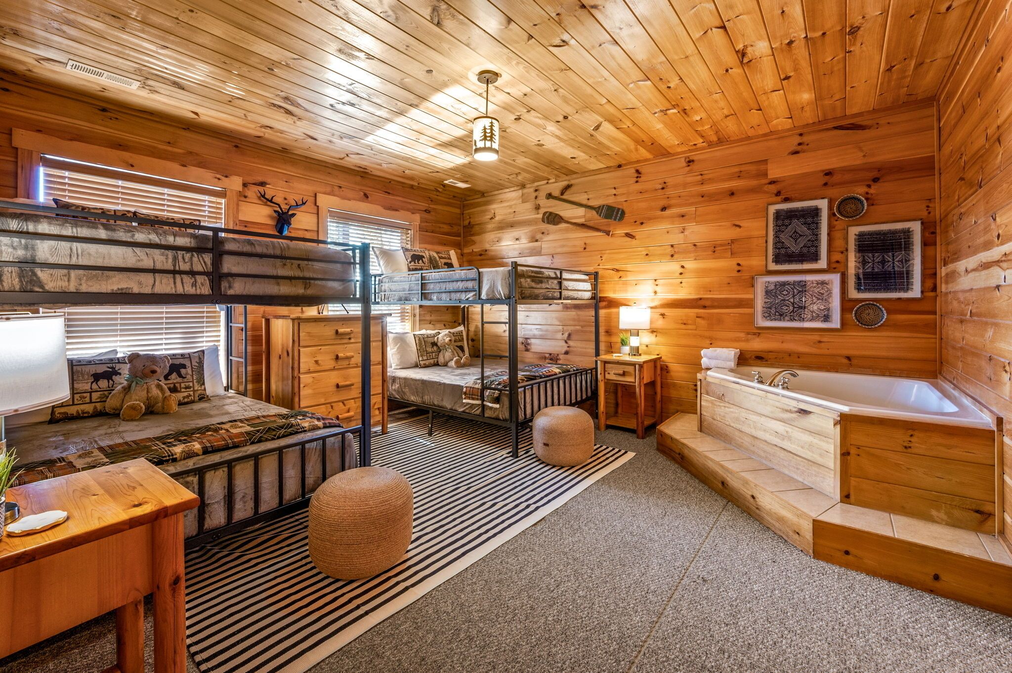 A cozy cabin interior with a bunk bed, a bathtub, a wooden desk, and a window with blinds.