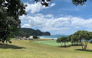 Uma quadra de tênis rodeada por árvores e uma praia ao fundo.