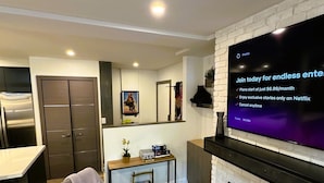 Una sala de estar moderna con un televisor de pantalla plana montado en una pared de ladrillo blanco, una chimenea y un sillón gris.