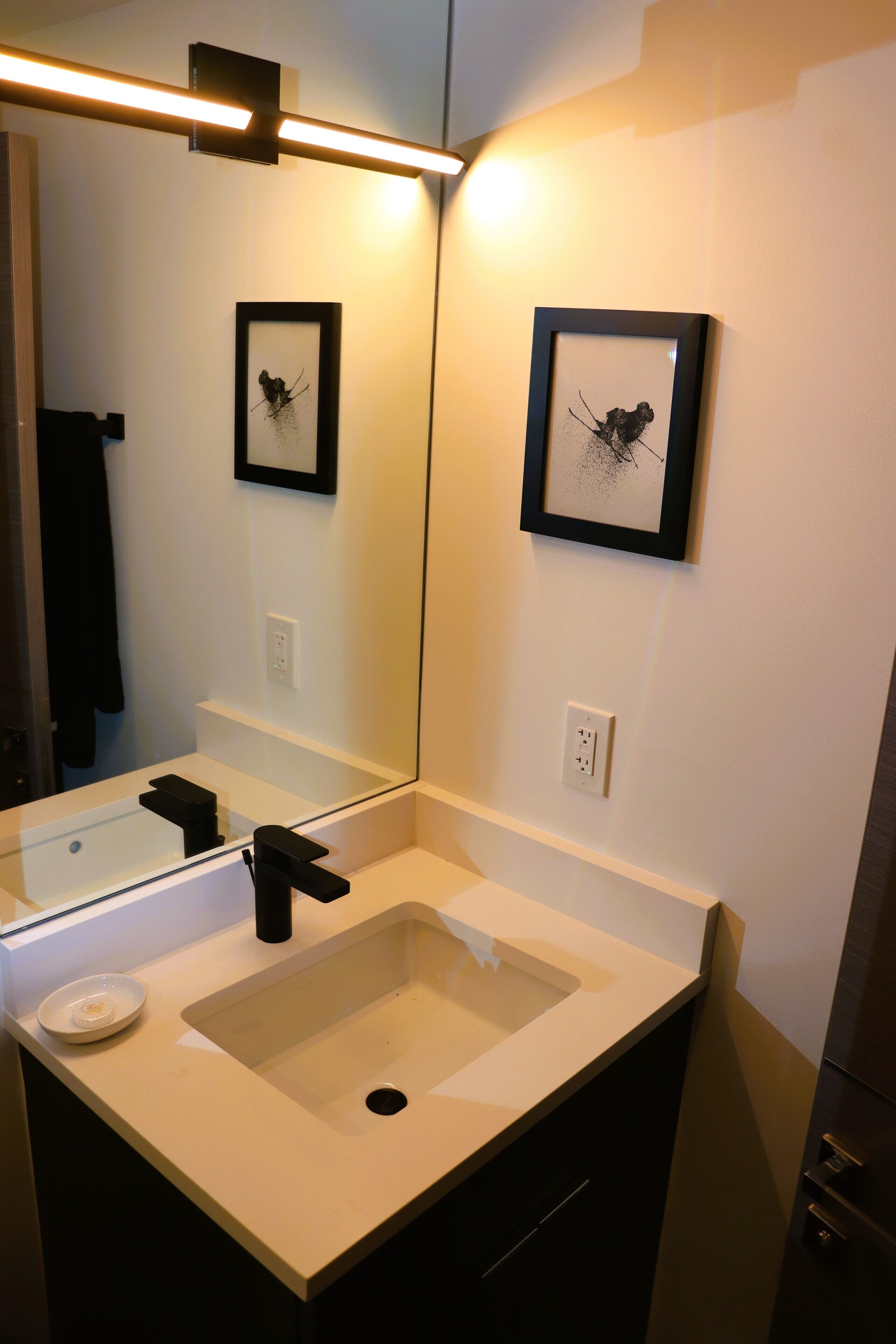 A bathroom with a large mirror, a sink, and two framed pictures on the wall.