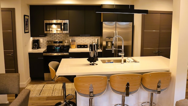 Una cocina moderna con armarios oscuros, electrodomésticos de acero inoxidable y una isla central con taburetes de bar.
