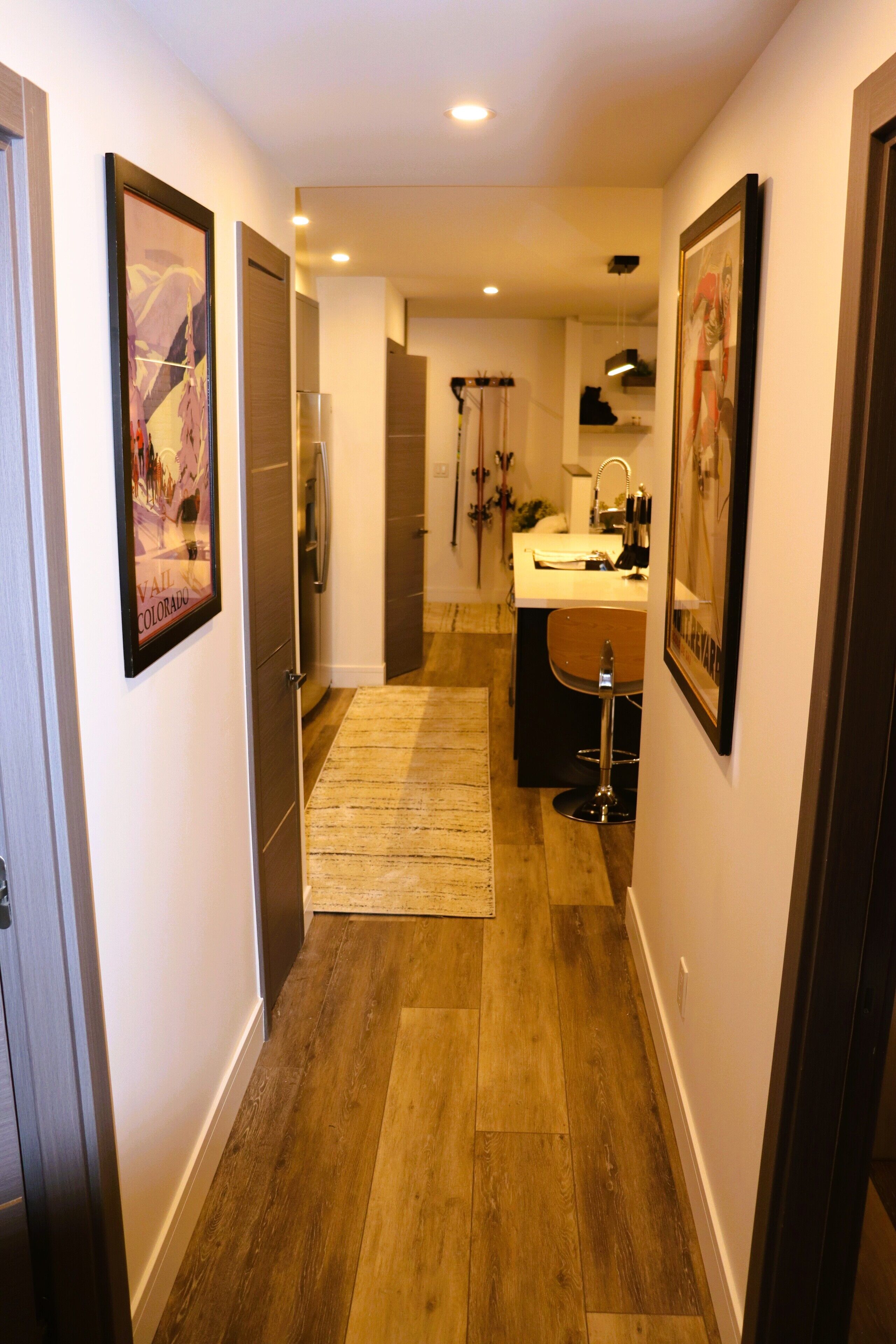 A hallway with wooden flooring, a rug, and framed pictures on the walls.