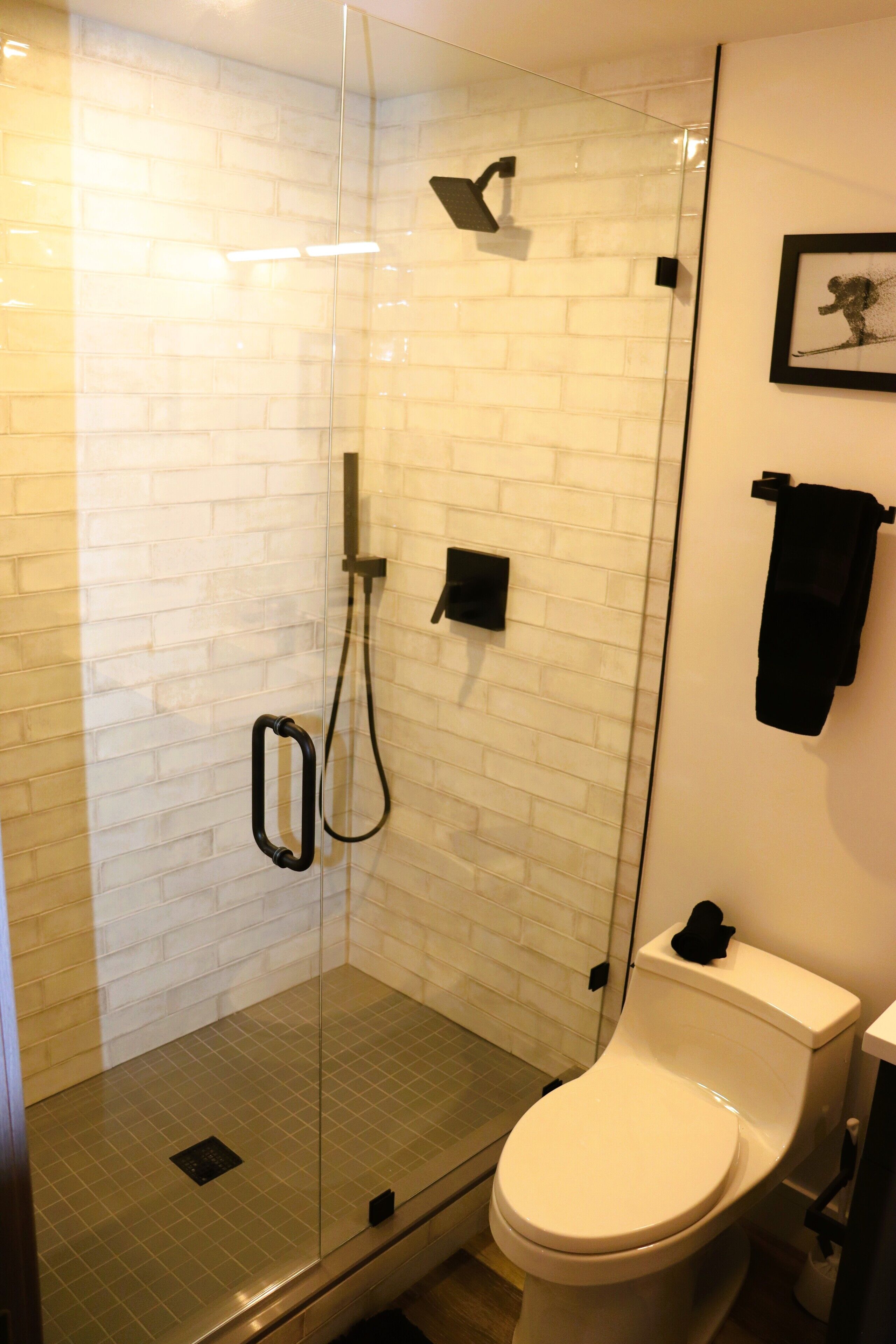Ein modernes Badezimmer mit einer gläsernen Duschkabine, einer weißen Toilette und einer gefliesten Wand.