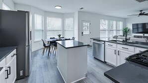 A modern kitchen with a central island, white cabinetry, and a dining area with a table and chairs. - Newly Renovated Luxury 5BR – Family & Game Room (The Colony)