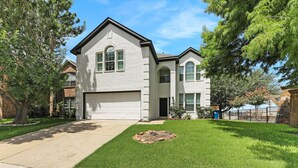 A two-story house with a garage, a well-maintained lawn, and a brick fire pit. - Newly Renovated Luxury 5BR – Family & Game Room (The Colony)