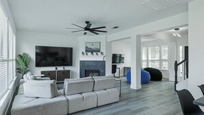 A modern living room with a grey sectional sofa, a flat-screen TV, a fireplace, and a ceiling fan. - Newly Renovated Luxury 5BR – Family & Game Room (The Colony)