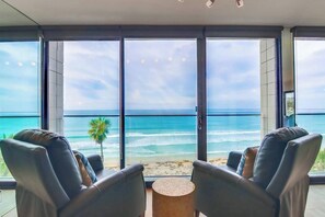 A room with a view of the ocean, two leather chairs, and a small round table.