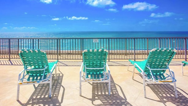 Drie groene stoelen gericht op een strand met een heldere lucht.