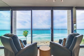 A room with a large window overlooking a beach, two leather chairs, and a small round table.