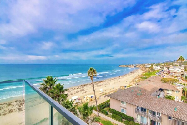 A coastal view from a balcony overlooking a beach with a clear sky.