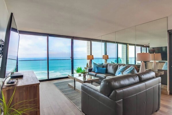 A modern living room with a large window overlooking the ocean, a leather sofa, a coffee table, and a TV.