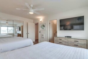 A hotel room with a large bed, a ceiling fan, a flat-screen TV, a wooden dresser, and a wall-mounted artwork.