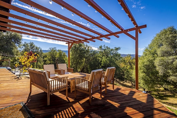 A wooden deck with a pergola, outdoor furniture, and a view of trees and hills.