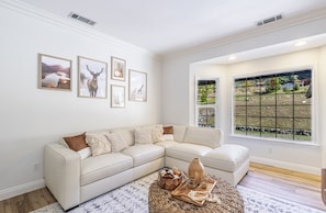 A living room with a white sectional sofa, a wooden coffee table with decorative items, and framed pictures on the wall.