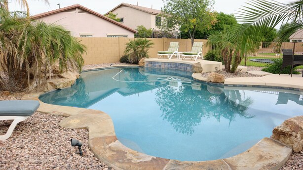 Una piscina con lettini, una vasca idromassaggio e un giardino curato.