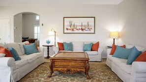 A living room with two white sofas, a wooden coffee table, and a painting of cacti on the wall.