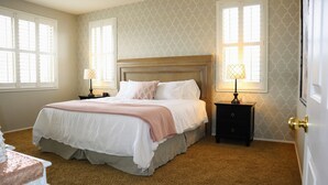 Un letto rifatto con una coperta bianca e rosa, due comodini con lampade e una carta da parati decorata.
