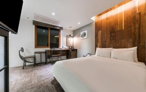 A hotel room with a large bed, a desk with a chair, a window, and a wooden accent wall. - Hotel DAYS.A (Busan)