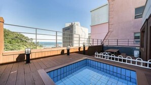 Una piscina al terrat amb vistes al mar, envoltada d'una terrassa de fusta i una barana metàl·lica.