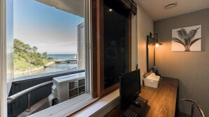 Habitació amb vista a un paisatge costaner, una taula amb un ordinador i una làmpada penjada a la paret.