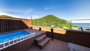Una piscina al terrat amb fusta, vista a un turó verd i al mar, i una tanca de fusta.