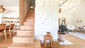 Amplia sala de estar con una escalera de madera, una pared de piedra blanca y un rincón de descanso acogedor con sofá y mesa de centro.