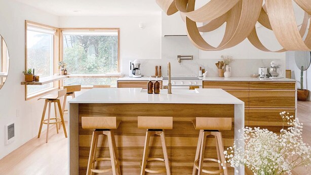 Cocina moderna con una isla central, taburetes de madera, cafetera y vistas a zonas verdes por la ventana.