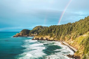 A coastal landscape with a forested hillside, a beach, and a lighthouse. - Ocean View, Perfect for Agate Hunting! Dog Friendly! Fireplace! (Florence)
