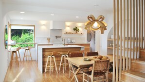 Una cocina moderna con suelo de madera, una isla central, taburetes de bar y una mesa de comedor con sillas.