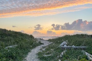 A coastal path with grass and driftwood, leading to the sea under a sunset sky.