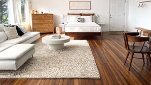 Une chambre à coucher moderne avec un grand lit, un canapé blanc, une table basse ronde et un plancher en bois.