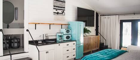A compact, modern room with a kitchenette, a bed with a teal blanket, and a large window with curtains.