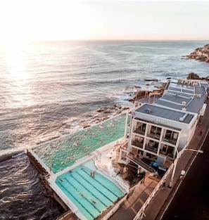A coastal hotel with a swimming pool, a building with balconies, and a view of the ocean. - Bondi Beachside Apartment: 3 Bedrooms & Parking (Bondi Beach)