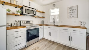 A modern kitchen with white cabinets, a microwave, oven, and wooden countertops. There is a window with a view of the outside, and a motivational quote on the wall. - 1 Mi to Gulf Coast! Couples Retreat in Long Beach (Long Beach)