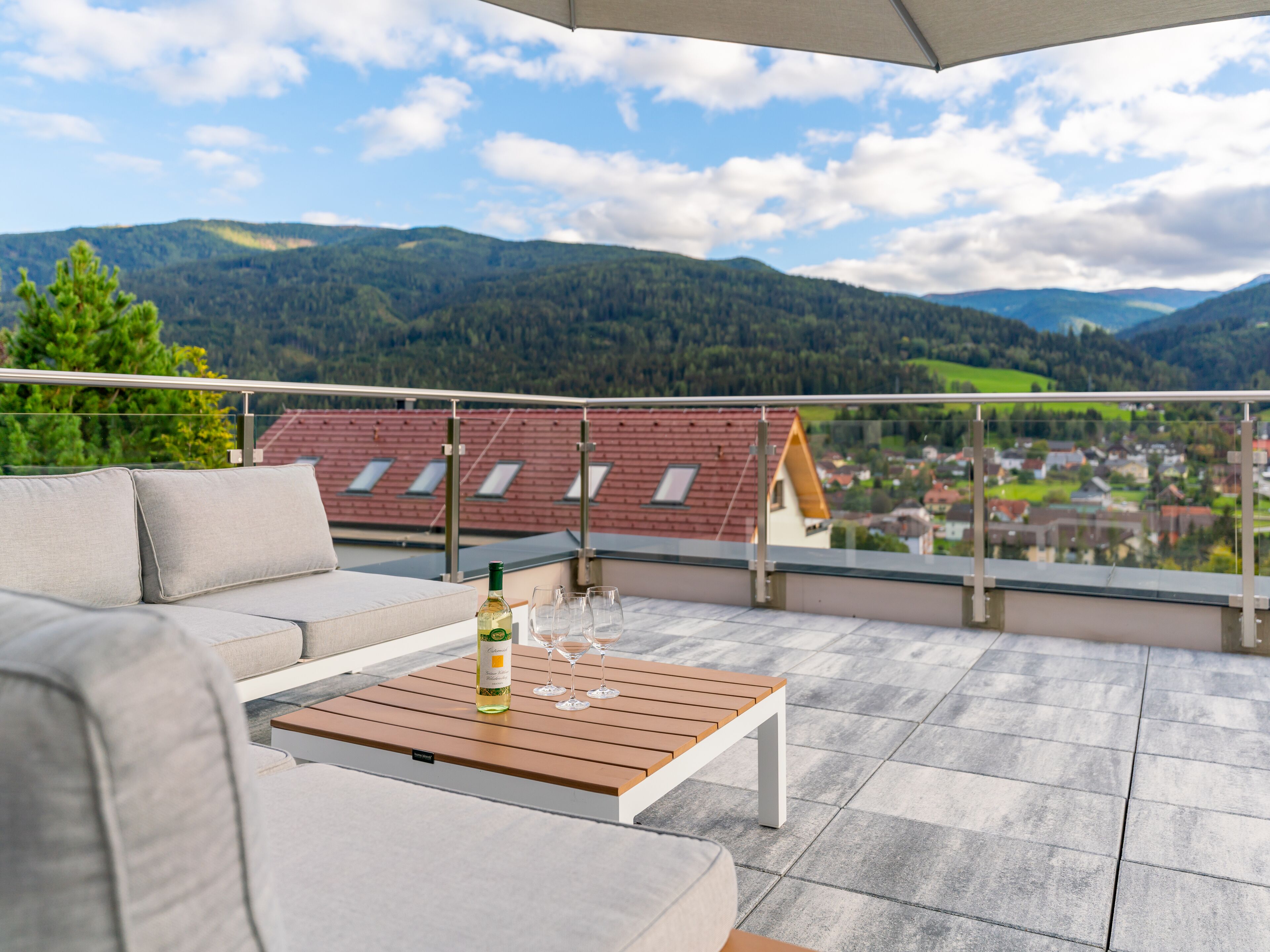 A balcony with a sofa and a table, a bottle of wine, and wine glasses.
