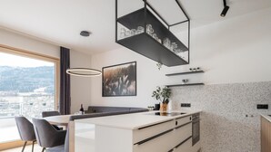 Cocina moderna con una isla central, estanterías oscuras arriba y vistas a la ciudad a través de amplios ventanales.