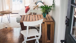 A cozy room with a wooden table and white chair, a ceiling fan, a door with a view to the outside, and a small plant on the table.