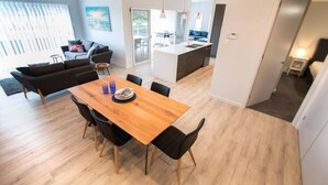 Eine moderne Küche mit einer zentralen Kochinsel, einem Essbereich mit einem Holztisch und schwarzen Stühlen sowie einem Wohnbereich mit einer Couch und einem Couchtisch.