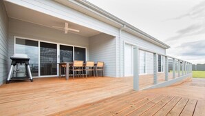 Ein überdachter Außenbereich mit Holzdeck, Grill und Tisch mit Stühlen.