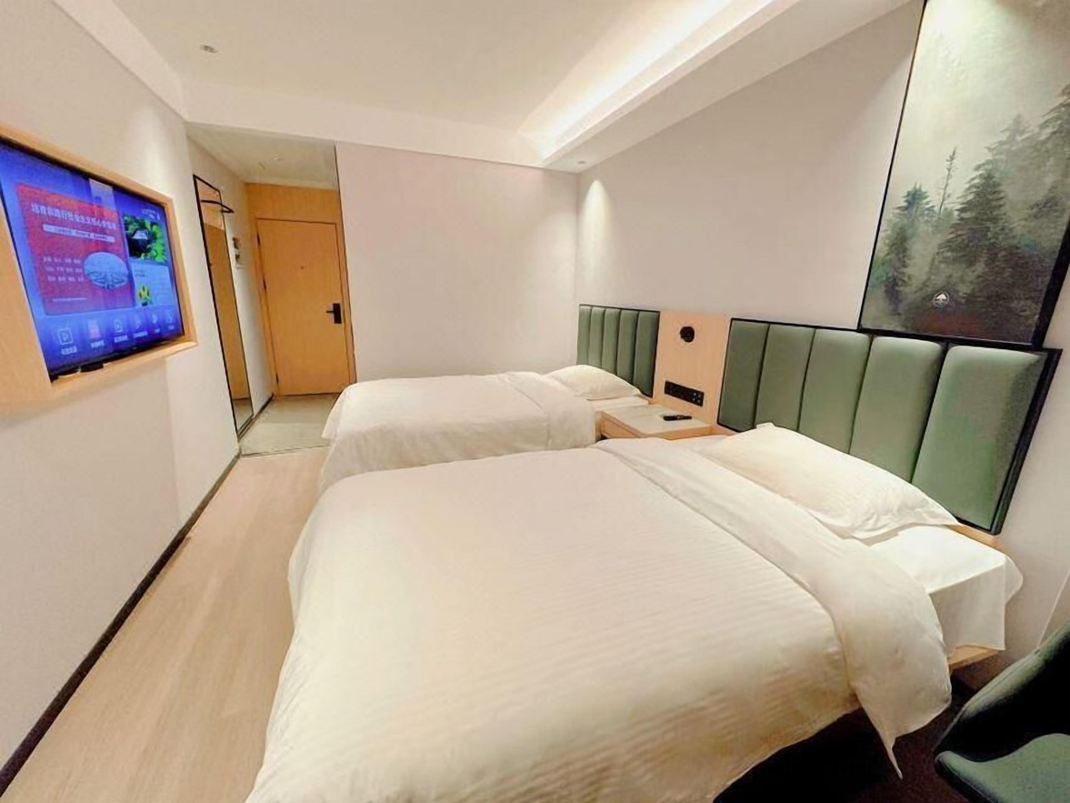 Una habitación de hotel con dos camas, un televisor montado en la pared y un cuadro colgado.