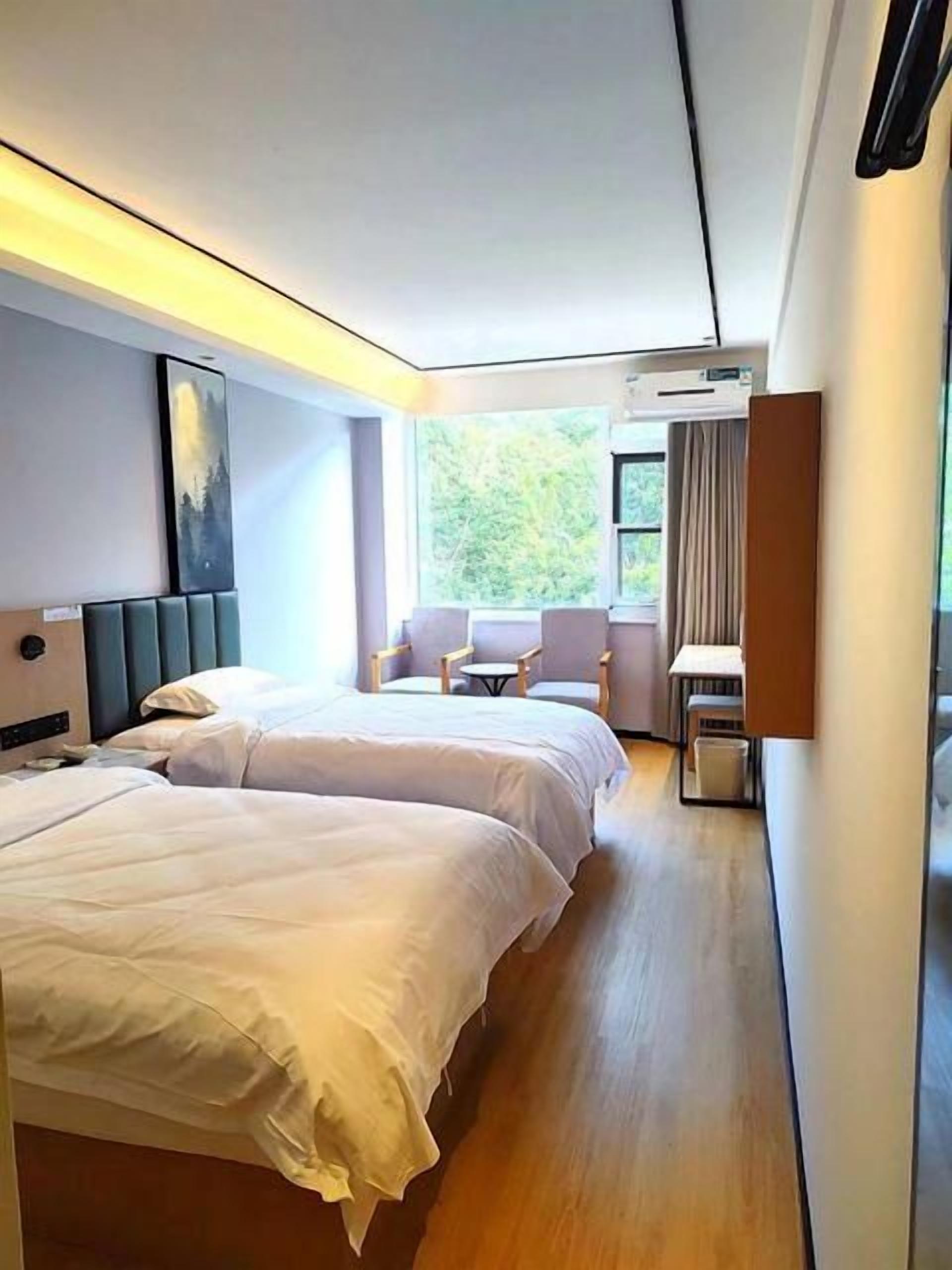 A hotel room with two beds, a seating area with chairs, a small table, and a window with a view of greenery.