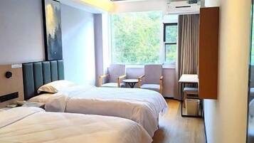 A hotel room with two beds, a seating area with chairs, a small table, and a window with a view of greenery.