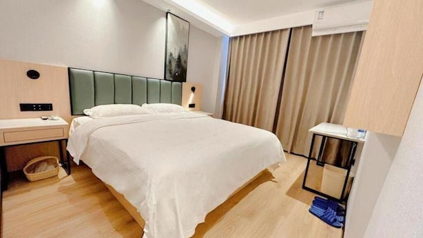 A hotel room with a large bed, a bedside table, a lamp, a small table with a bottle, and a window with curtains. - Greentree Inn Langfang Guangyang District Guangyang Avenue North Yongxing Road Express Hotel (Langfang)
