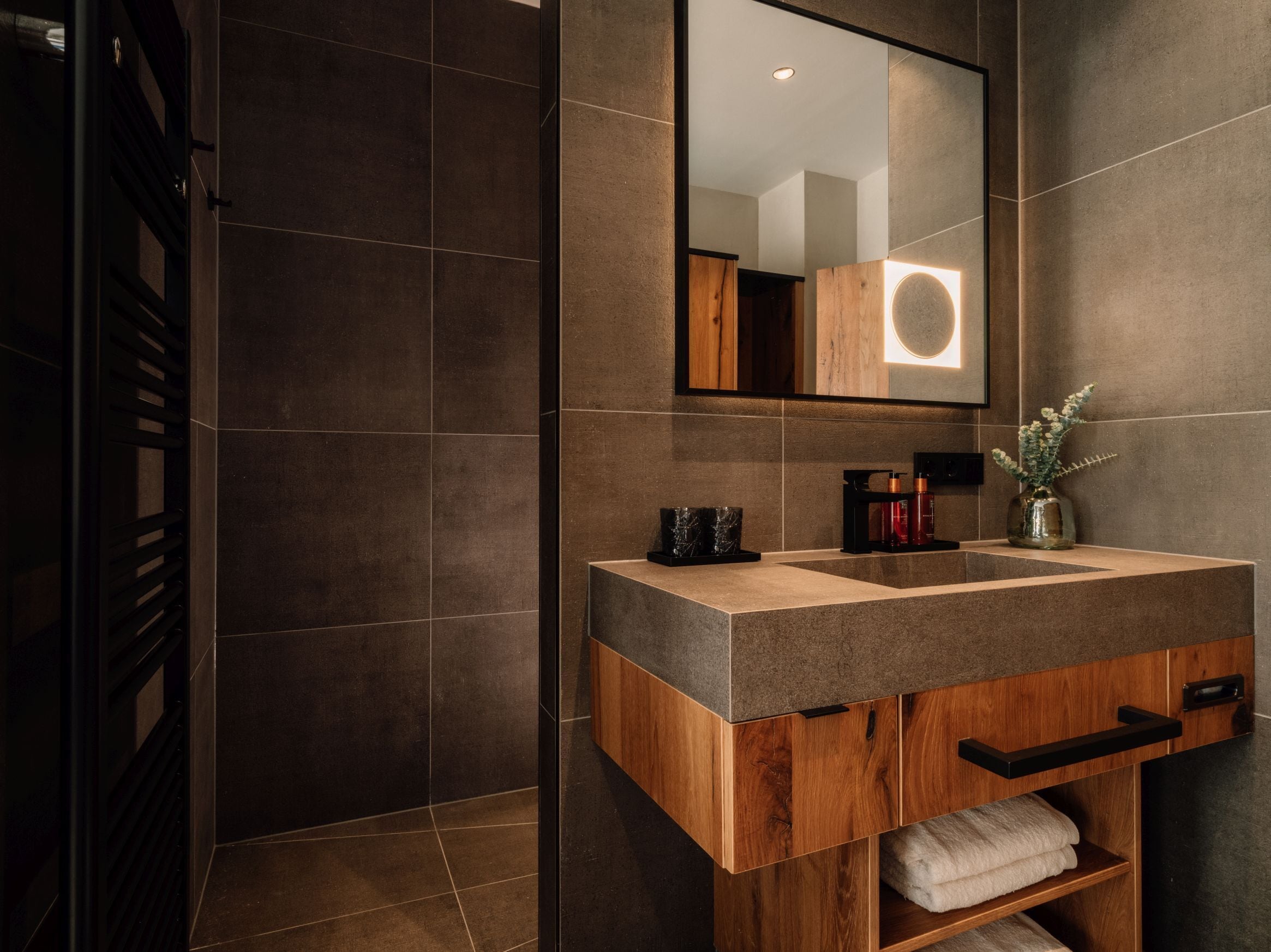A modern bathroom with a wooden vanity, a large mirror, and a built-in towel rack.