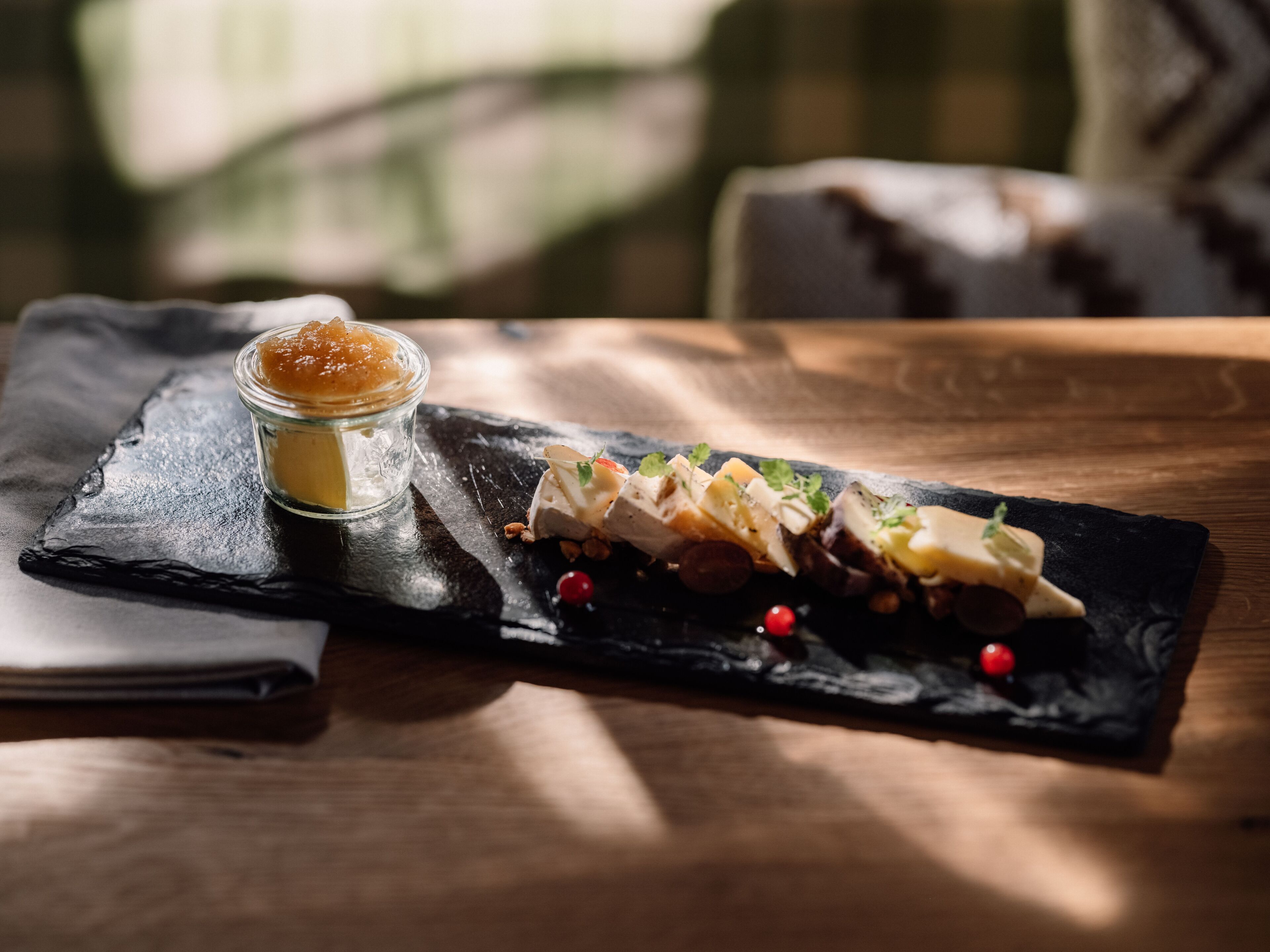 A dessert platter on a slate board with a small jar of jam and scattered berries.