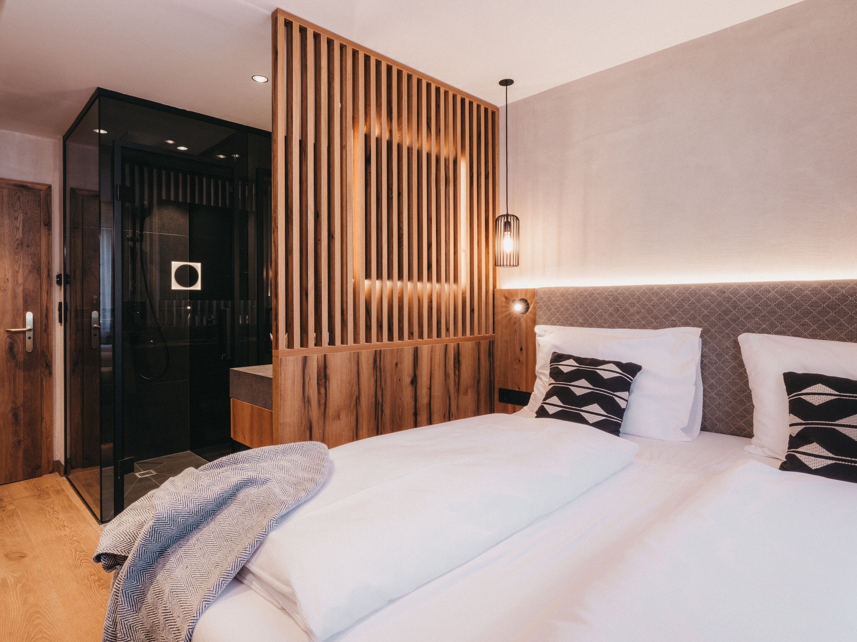 Habitación de hotel moderna con una cama grande, un panel de pared de madera y una puerta de vidrio que da a un baño.
