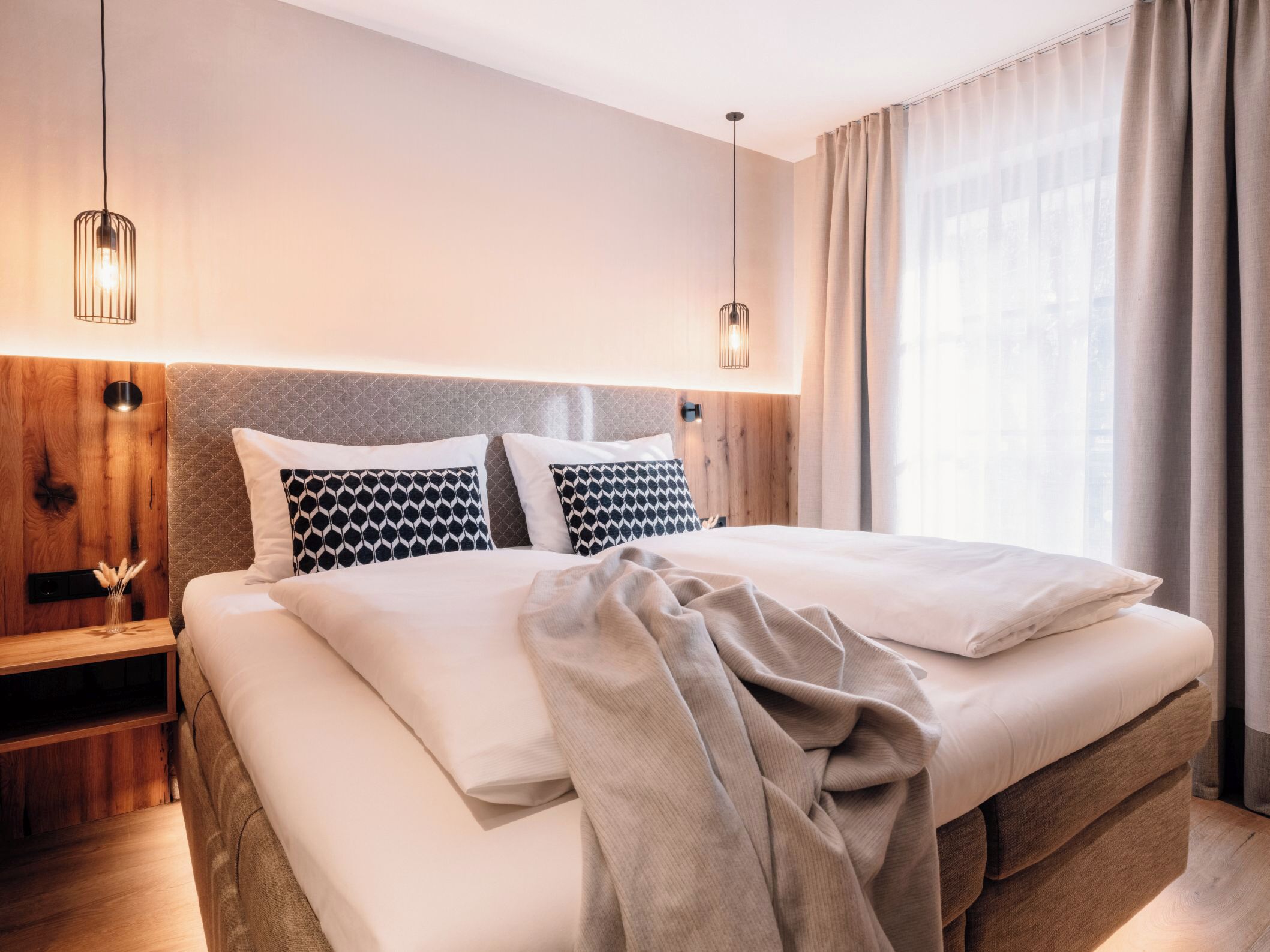 A modern hotel room with a large bed, wooden headboard, and a nightstand with a lamp.